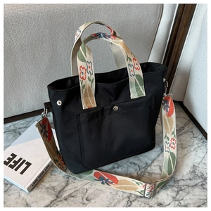 Detail of black nylon tote bag with floral embroidered handles and metal snap pocket