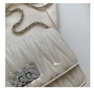 Close-up of quilted stitching and silver twist lock on a beige crossbody chain bag
