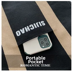 Detail of a striped canvas tote bag showing a functional front pocket with a smartphone