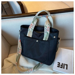 Close-up of black nylon tote bag featuring vibrant floral embroidery and metal buckle
