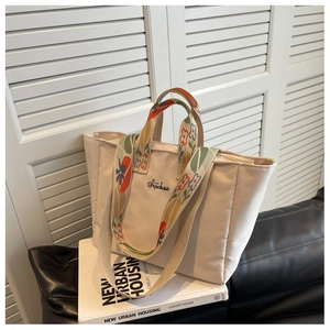 Dettaglio della borsa tote in tela crema con spalline floreali e logo ricamato