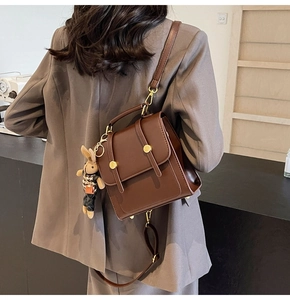 Close-up of vintage brown leather mini backpack with a cute bunny charm on a grey suit