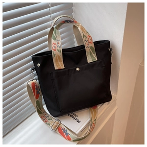 Detail of black nylon tote bag featuring floral embroidered straps and silver metal snap button