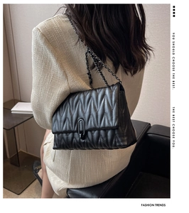 Detail of black quilted chain shoulder bag with metal U-shaped buckle and V-stitch pattern