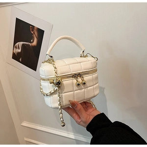Detail of white quilted handbag featuring premium gold chain strap and spherical charm