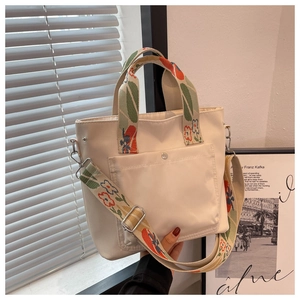 Detail of white nylon tote bag featuring colorful floral woven straps and front buckle pocket