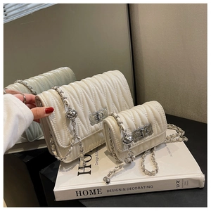 Close-up of wavy quilted shoulder bags in ivory with silver chain straps and ball charm