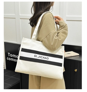 Détail du grand sac cabas en toile blanche à rayures noires porté par un mannequin