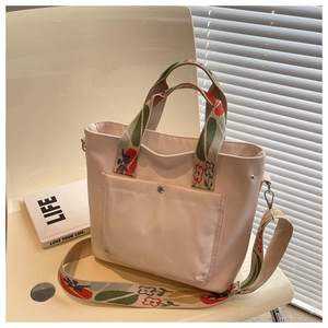 Detail of a beige nylon tote bag with floral embroidered handles and adjustable strap