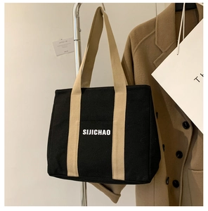 Detail of black canvas tote bag with beige handles and white logo for daily commute
