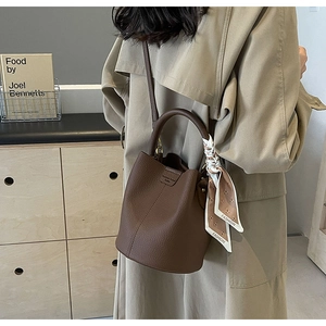 Detail of a dark brown pebble leather bucket bag with fashion print scarf on handle