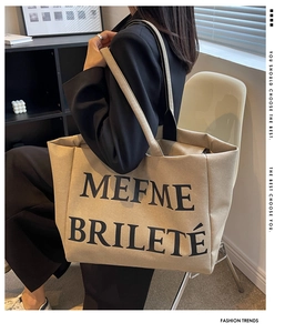 Porté épaule d'un grand sac cabas en toile beige avec anses noires et texte artistique