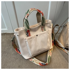 Detail of cream tote bag featuring floral embroidered wide straps and metal buckle pocket