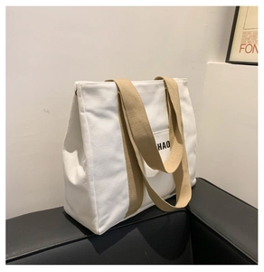 Close-up of a white canvas tote bag with khaki wide handles and HAO logo on a black sofa