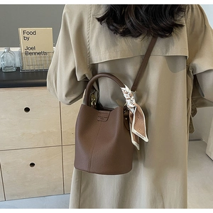 Brown lychee leather bucket bag detail with a silk scarf wrapped around the handle