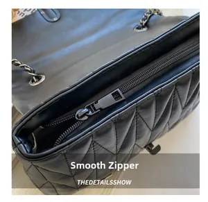 Detail shot of the smooth metal zipper and quilted leather texture on the black handbag