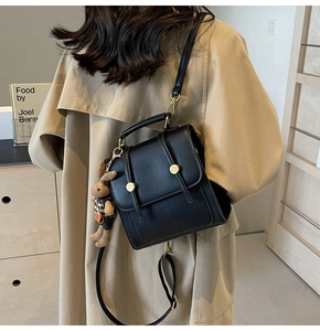 Detail of a black square backpack with vintage buckles and a small rabbit doll accessory