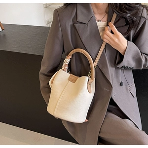 Detail of a beige pebbled bucket bag with brown handle and decorative silk scarf
