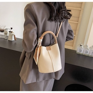 Detail of a beige bucket bag with brown handles, decorative scarf and lychee texture