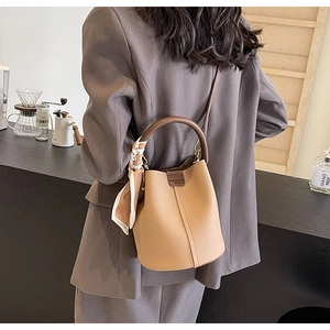 Detail view of khaki bucket bag with floral scarf and contrast handle in a cafe setting