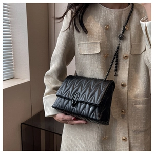 Close-up of black quilted shoulder bag with matte metal clasp and chain strap detail