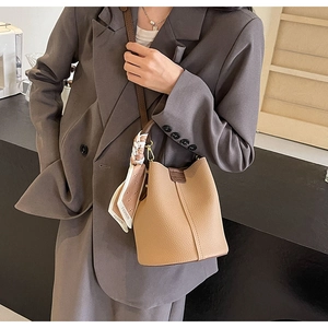 Detail of light camel bucket bag with lychee texture leather and decorative silk scarf