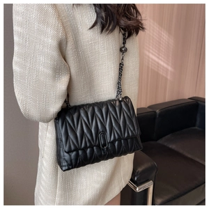 Detail of black quilted crossbody bag with wave texture and metal chain on model
