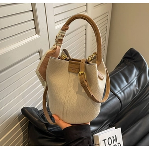 Macro shot of a cream leather bucket bag with a silk scarf detail and brown handle
