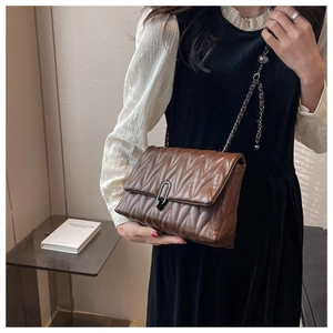 Close-up of brown quilted shoulder bag featuring V-stitch pattern and black metal chain