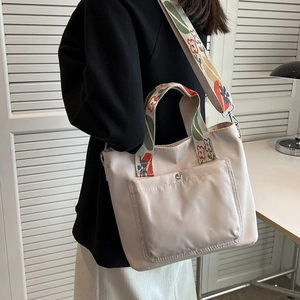 Beige nylon tote bag with floral embroidered strap shown on model against white background