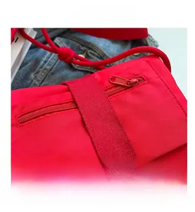 Detail view of red nylon crossbody bag showing zipper pocket and wide webbing strap