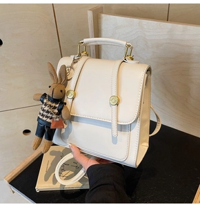 Close-up of a cream-white leather backpack with golden buckles and a rabbit charm