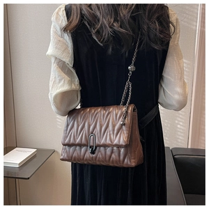 Detail of dark brown quilted chain bag featuring wavy stitching and metallic U-shaped buckle