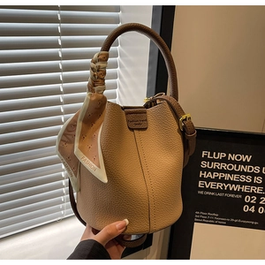 Detailed view of light brown leather bucket bag with silk scarf wrapped on handle