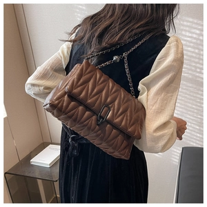 Detail of dark brown quilted leather crossbody bag with chain strap on a model