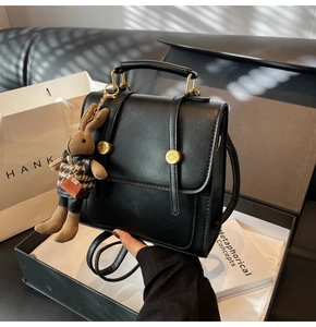 Detail of black structured handbag with gold hardware and a cute bunny plush charm on display