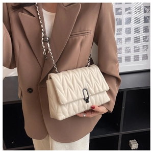 Detail of cream quilted handbag featuring a black metal clasp and chain strap on a blazer