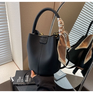 Detail view of a black lychee grain leather bucket bag with silk scarf on the handle
