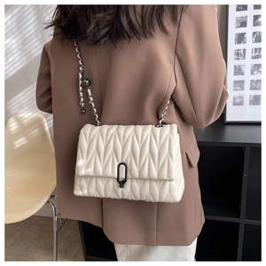 Detail of cream quilted chain bag with black oval buckle and metallic woven strap