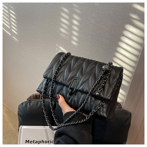 Detail of black quilted leather shoulder bag with dark grey metal chain and ball charm