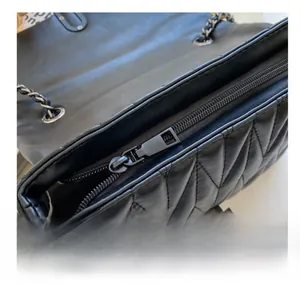 Detailed macro view of the smooth metal zipper and quilted leather on this black crossbody bag