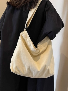 Minimalist beige canvas tote bag with adjustable shoulder strap worn on black outfit