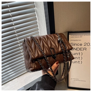 Detail of dark brown quilted crossbody bag featuring V-shaped stitching and chain strap