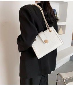 Detailed view of white crocodile pattern shoulder bag with gold chain strap on a black blazer