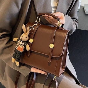 Vintage brown leather backpack with rabbit charm and gold buckles in a stylish outdoor setting