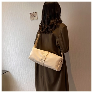 Beige nylon cylindrical crossbody bag shown with a brown coat on a model in a minimalist setting