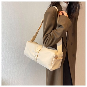 Detail of a large beige nylon crossbody bag featuring a wide strap and cylinder shape