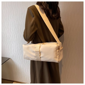 Close-up of cream nylon cylindrical crossbody bag with adjustable strap on model