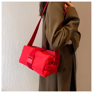 Side view of a bright red nylon cylinder crossbody bag on a model wearing an overcoat