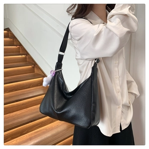 Detail of black lychee leather crescent bag with silver buckle and plush charm decoration